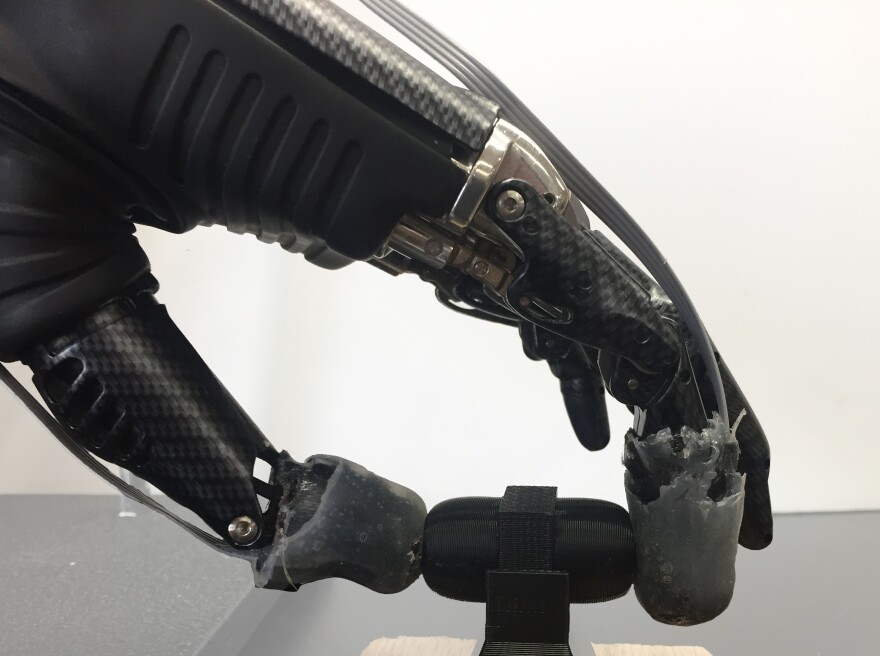 A prosthetic hand grips an object with synthetic skin on its fingertips.