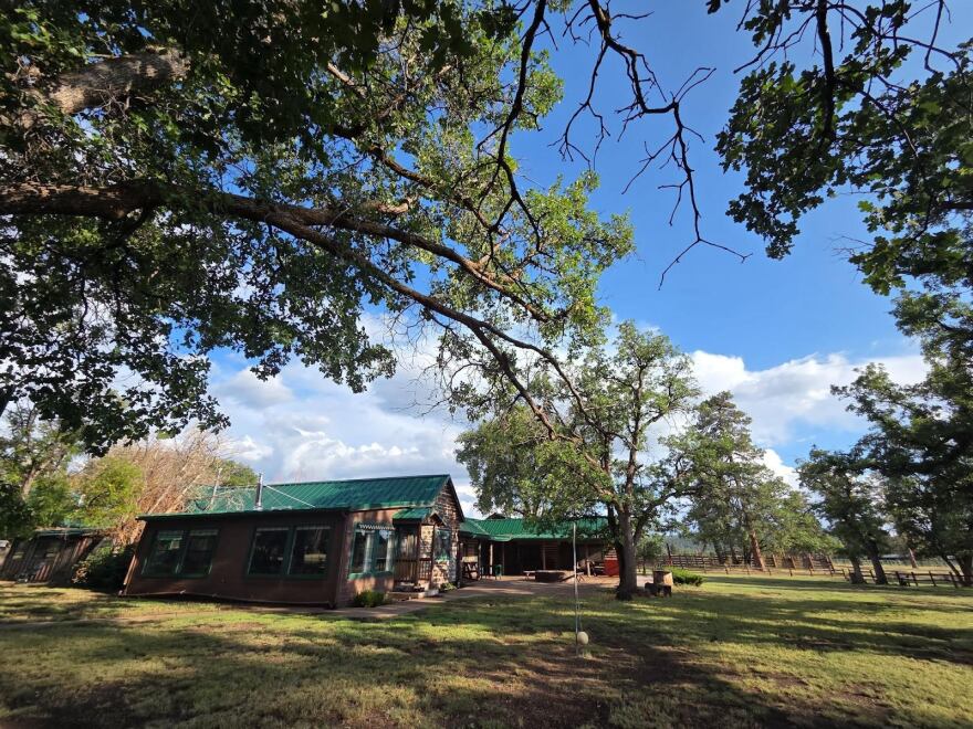 A ranch building with a green roof beneath large trees