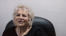 A woman in a black shirt and pearl necklace smiles.