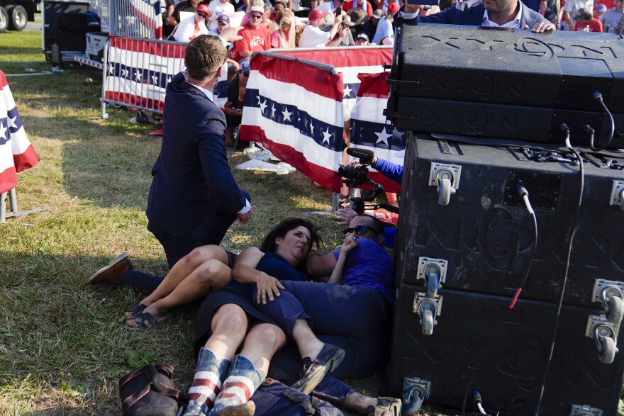 People take cover as U.S. Secret Service agents surround Republican presidential candidate former President Donald Trump on stage at a campaign rally, Saturday, July 13, 2024, in Butler, Pa.