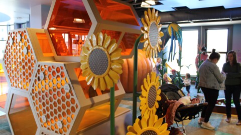 A giant honeycomb structure stands inside a room, with kids playing behind and parents standing. 