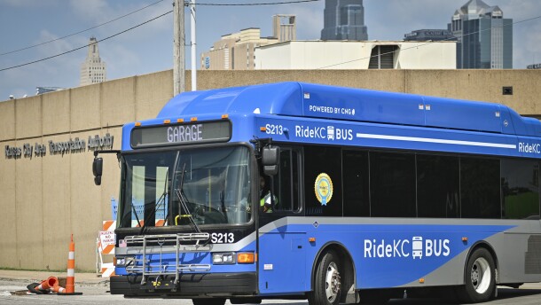 Exterior photo of a blue transit bus entering the street from a parking lot. Behind it is a building with a sigh that reads "Kansas City Area Transportation Authority."