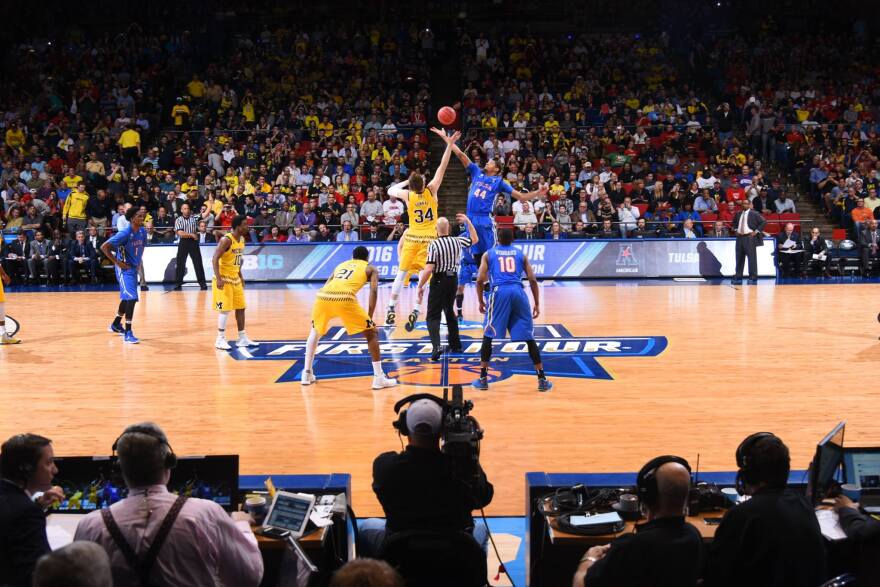 Basketball players wearing yellow and blue uniforms jump for the basketball in a packed arena.