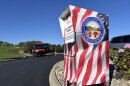 A ballot drop box designed to look like an American flag sits in a black asphalt parking lot.