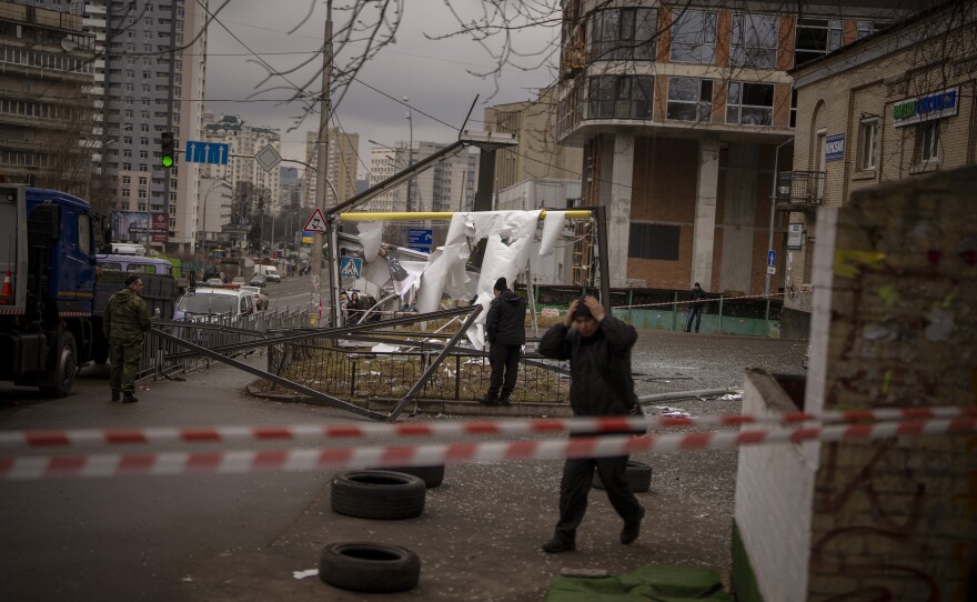 A person with their hands on their head walks past damage on a city street.