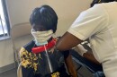 Health worker vaccinates Lolita Johnson, who is wearing a black and yellow dress, as she sits in a chair.