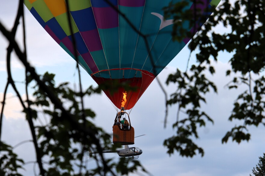A balloon called the Fleckfolly 5 soared overhead while passengers in a helicopter ride look on at the Suncook Valley Rotary's 44th annual hot air balloon rally on Friday July 31, 2026.