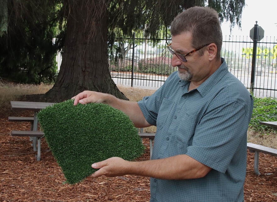 City of Eugene Landscape Architect Mark Kosmos holds a sample of the artificial turf.