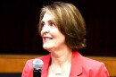 woman with short hair in peach-orange blazer holding microphone 