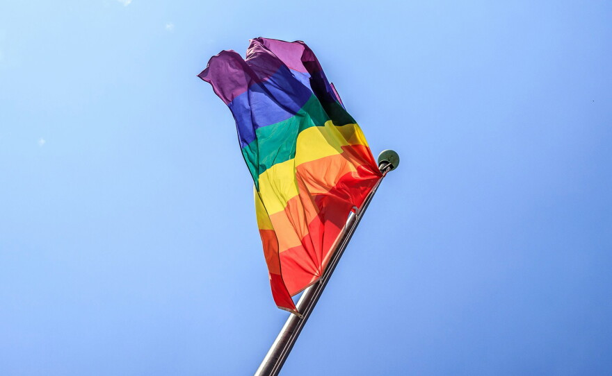 A pride flag on a flagpole with a blue sky background.