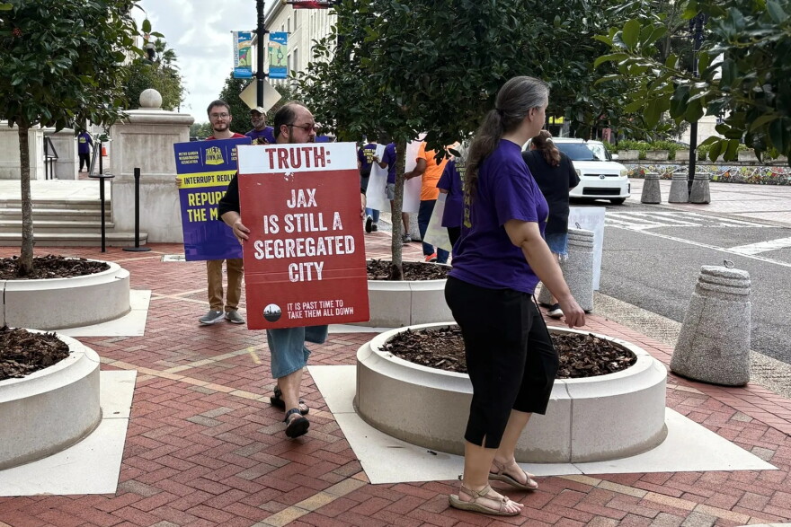 several protesters mark on brick floor park, one holds sign that says Trust: Jax is still a segregate city