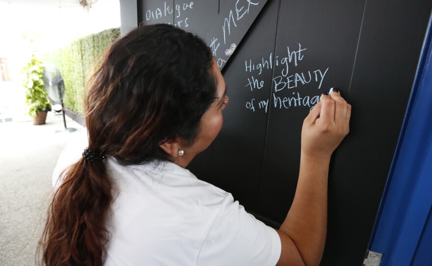 Ivette Diaz writes in chalk on one of the doors from the <em>Common Ground</em> installation. She is with the Libre Institute, one of the groups behind the project, which focuses on discussions around immigration.