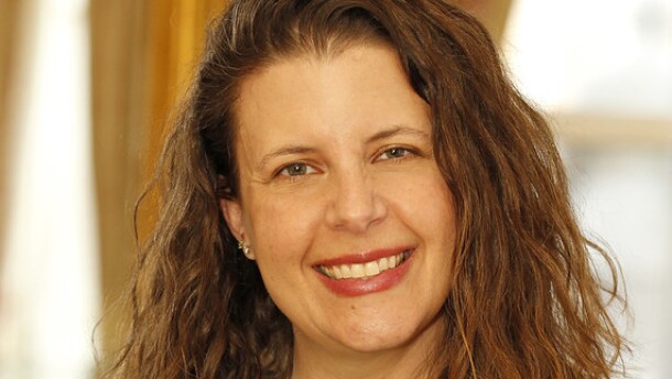 A smiling woman with curly brown hair, wearing a green blouse and a silver necklace