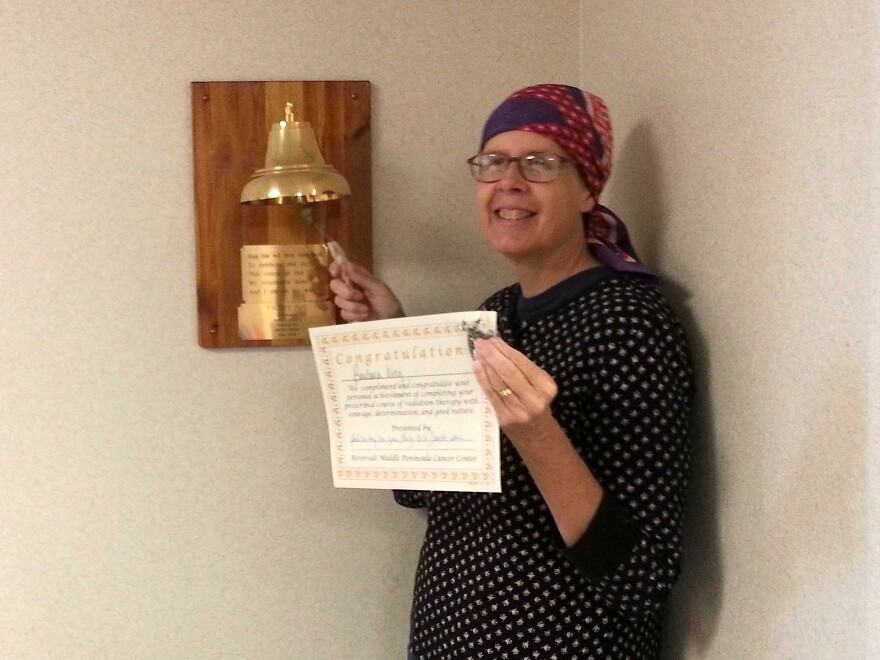 Barbara King rings the "victory bell" and holds up a certificate celebrating her completion of 25 external radiation treatments.