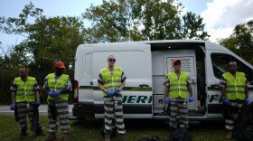 Members of Brevard County's chain gang stand in front of a Brevard County Sheriff's office van, wearing fluorescent green vests, blue gloves, black-and-white striped uniforms, and chains around their ankles.