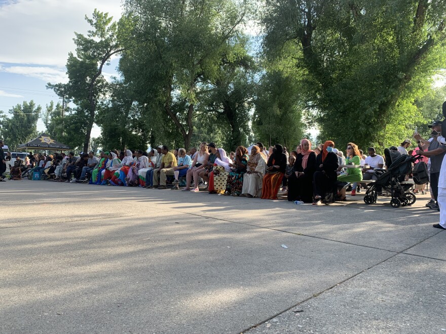 A long line of people in various traditional clothing sitting at a table to watch the dancing.