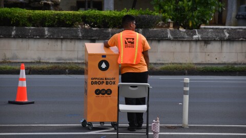 Staff member waits next to drive-by ballot drop box at Honolulu Hale.