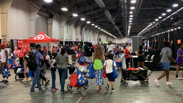lots of families and children in a lighted warehouse, many pulling filled wagons or with large colored bags in hand or over shoulders