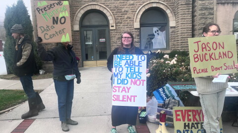 Several people holding hand made signs with messages including "I need to be able to tell my kids I did not stay silent" and "Jason Buckland please don't sell" and "Preserve Monroe no data center."
