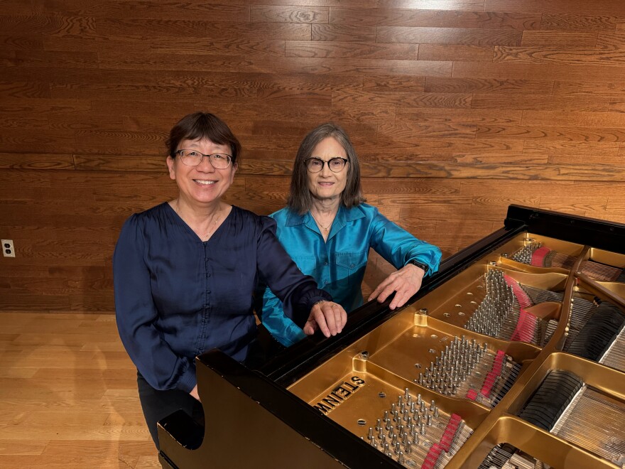 Two women sit at a piano, pictured from above