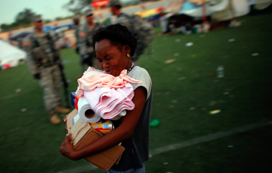 A Haitian woman smiles as she walks past soldiers from the 82nd Airborne after receiving her first ration of foreign aid, which has been coming in to a soccer stadium in Port-au-Prince, four days after the quake hit.