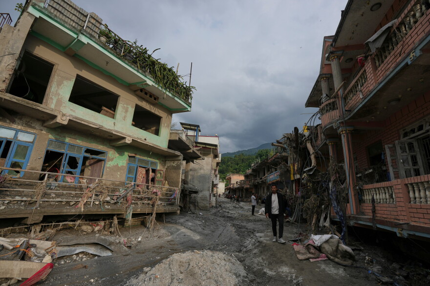 People walk along a street lined with damaged structures after flash flooding in the Devighat area of Nuwakot district in Nepal on Friday, Aug. 28, 2026.