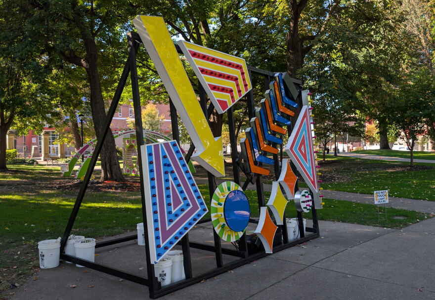 Brightly colored signs hang on a metal rack in a park during daylight hours.