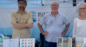 Three volunteers stand in the BPR booth with rack cards
