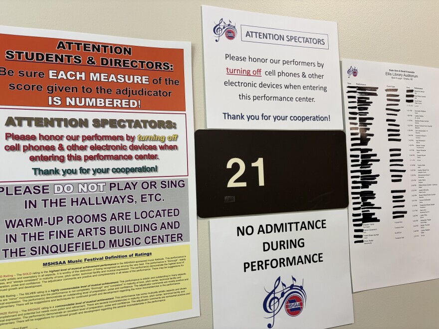 A photo of a signs outside of Ellis Library, outside of room 21. One of the signs says, "No Attendance During Performance."