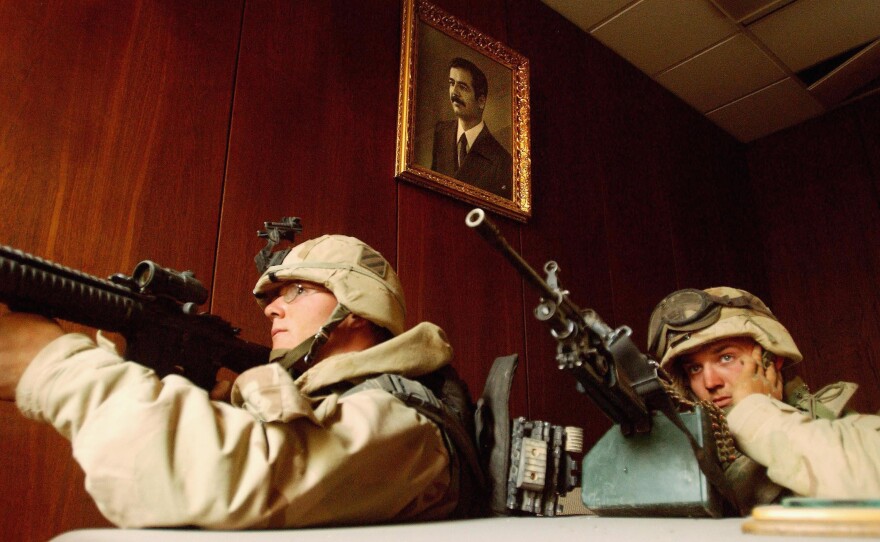 U.S. soldiers take cover near a portrait of Saddam Hussein while conducting a sweep of the VIP terminal of Baghdad International Airport on April 4, 2003.
