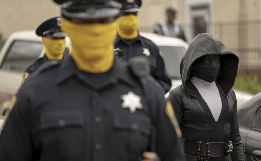 Police officers wear yellow fabric wrapped around their faces like masks, and King's character wears all black.