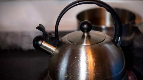 A stock photo of a kettle on a stovetop with boiling water releasing steam.