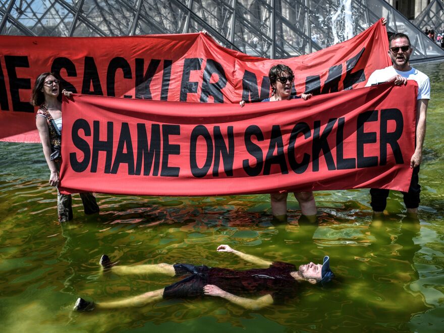 Activists hold banners reading "Shame on Sackler" and "Take down the Sackler name" in front of the pyramid of the Louvre museum in Paris in 2019.