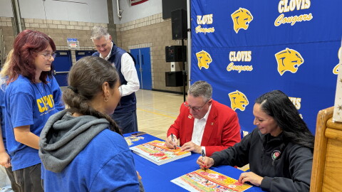 Terry Madigan, Tournament of Roses president, and Esmeralda Rocha Lozano, Clovis High music director, sign Rose Parade posters for band students.