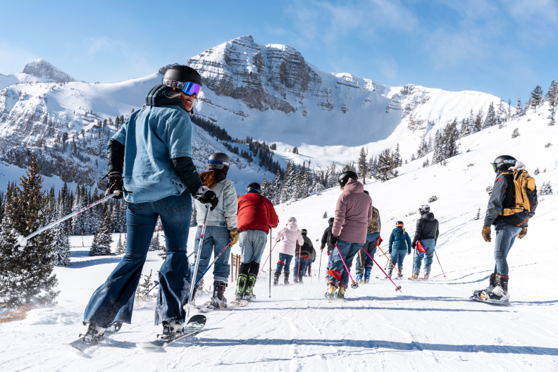 About a dozen people wearing jeans ski away from the camera