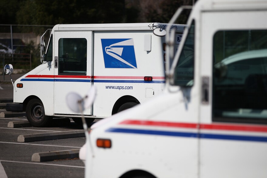 U.S. Postal Service mail vehicles sit in a parking lot at a mail distribution center.