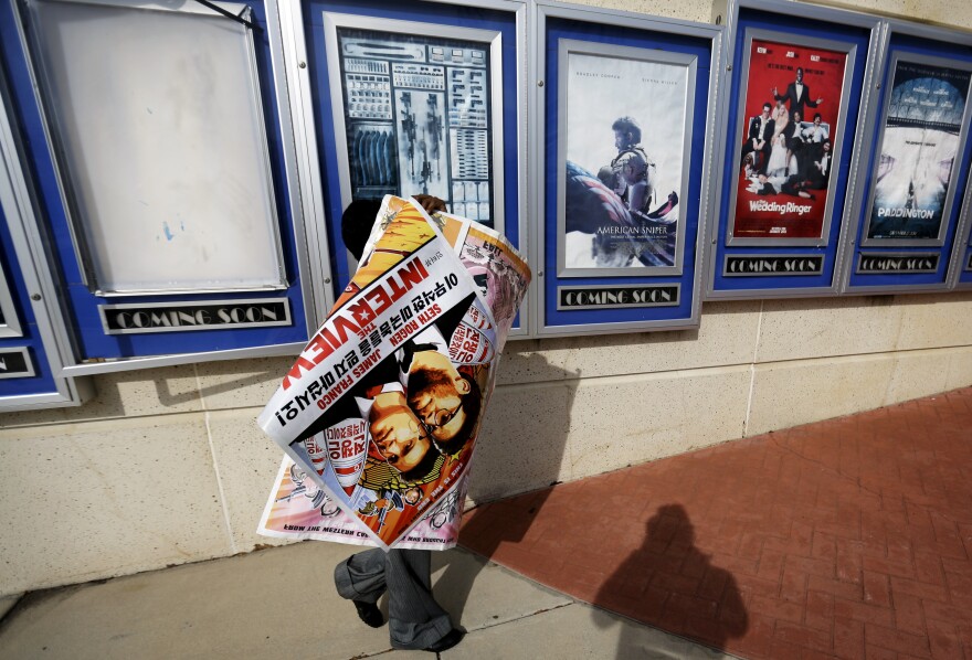 A worker carries a poster for the movie <em>The Interview</em> away from its display case at a theater in Atlanta. "It feels like the margin's narrowed about what kind of movies Hollywood will be making," says veteran Hollywood producer Stephanie Striegel.