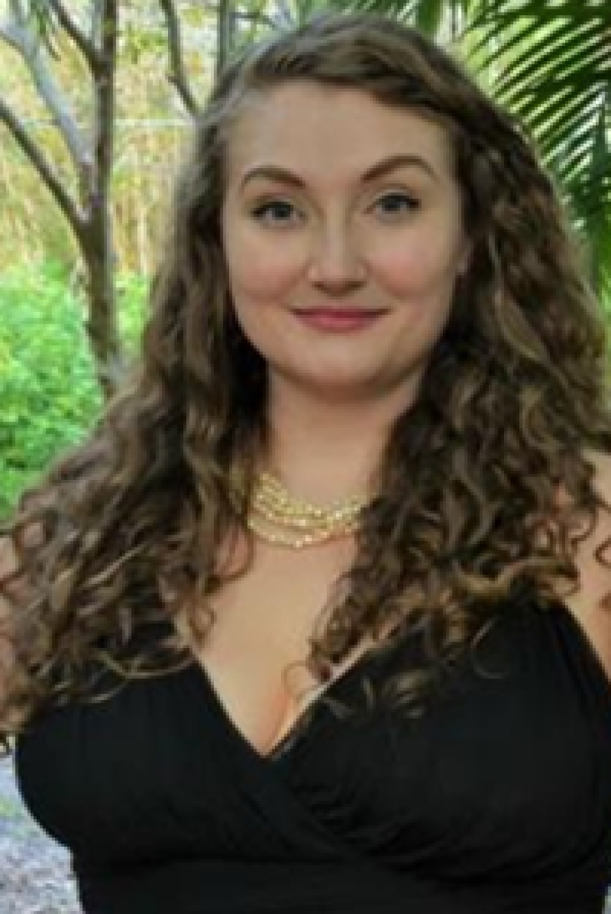 Woman with shoulder-length hair and black dress smiling into the camera