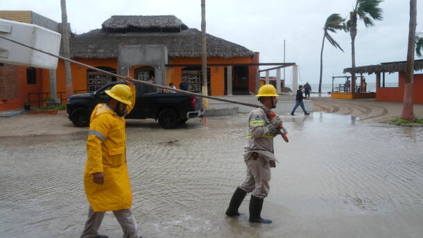 Workers in reflective jackets and rain boots pull a boat to shore in floodwaters in Mexico after Hurricane Polo blew through Baja California.