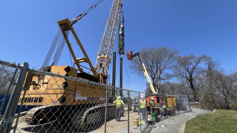 Workers prepare a diesel hammer to drive an H-pile into the ground on the southeast side of the Sagamore Bridge, adjacent to the former Christmas Tree Shops, to test the pile's performance in local soil and bedrock for a bridge foundation. Although testing is starting on the east side of the bridge, the new Sagamore Bridge will be build on the west side.