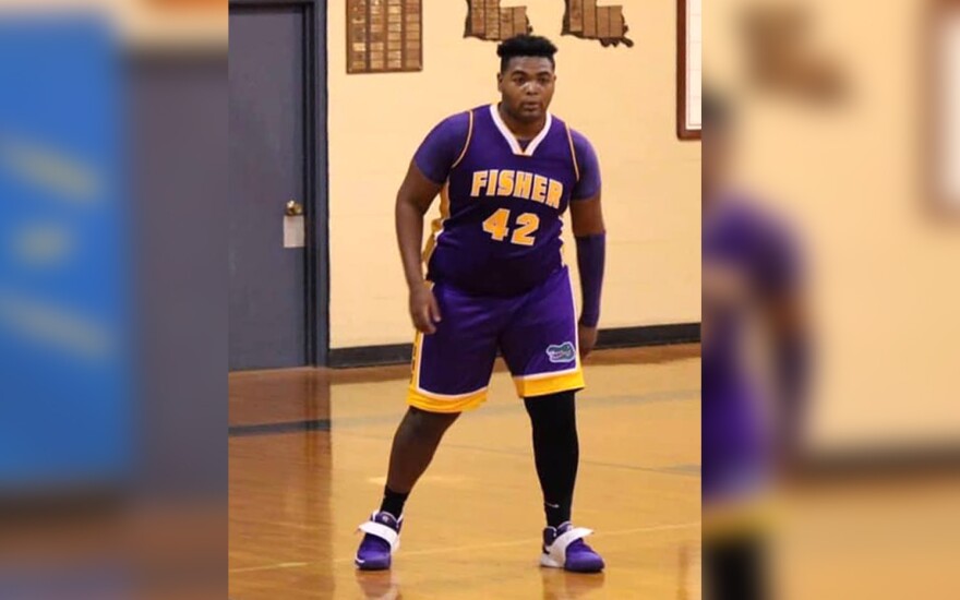 A young, Black man wearing a purple and yellow uniform with "Fisher 42" printed on the front stands on a basketball court.