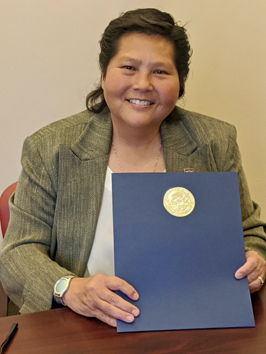 Headshot of Deborah Chang. She is holding a blue folder with a gold seal, looking toward the camera and smiling.