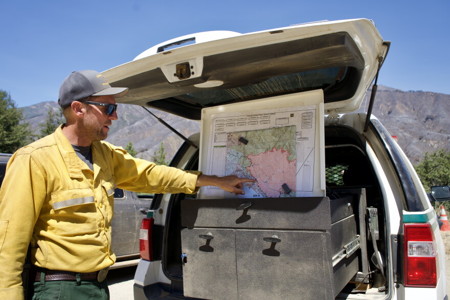 A man in a yellow jacket point  to a map in the back of a truck. 