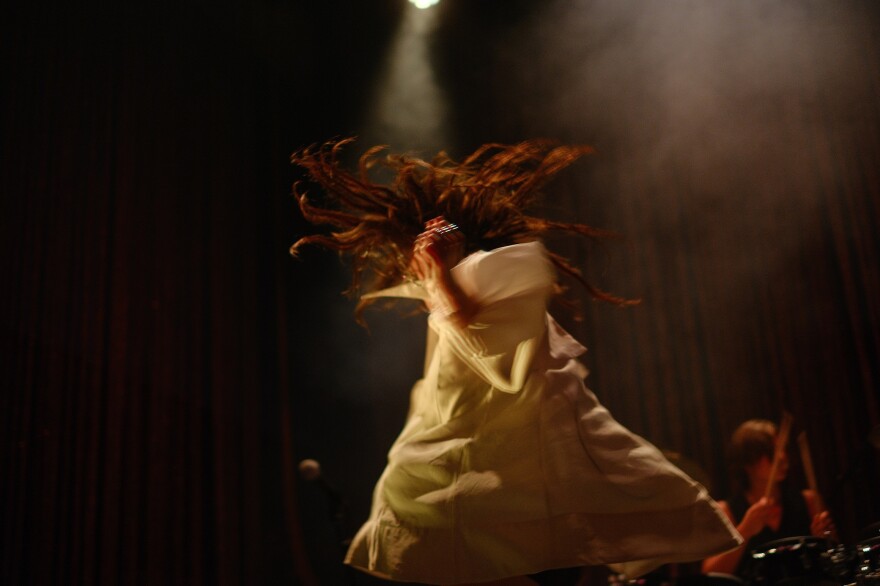 A woman spins on stage while performing at a concert venue, creating a blurring effect in the image.