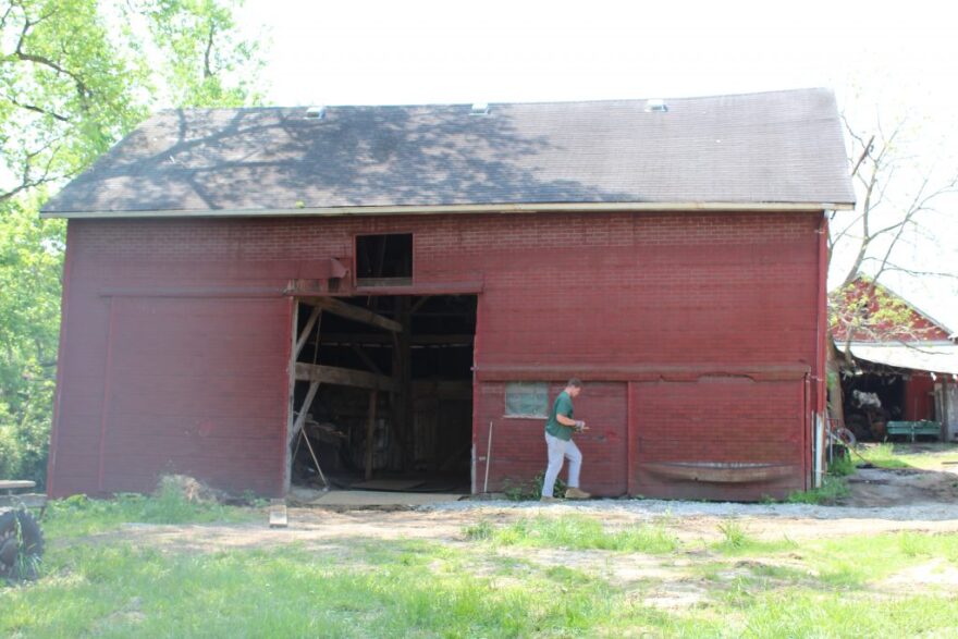man walks beside a red barn