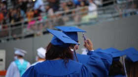 Teenagers walking away wearing blue caps and gowns.