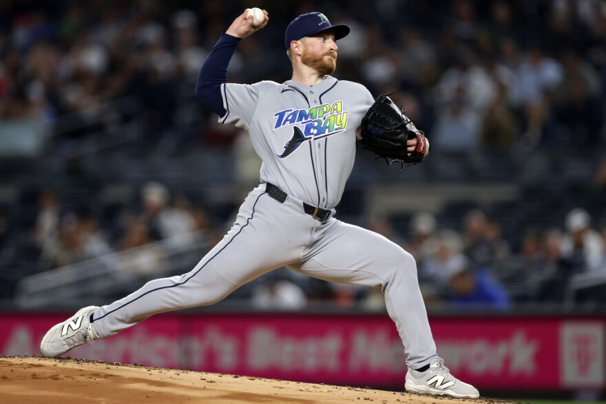 basball pitcher in motion on the mound about to throw a pitch. he's wearing a gray uniform with a jersey that says Tampa Bay with an image of a sting ray across the chest . and a blue cap with TB written on it 