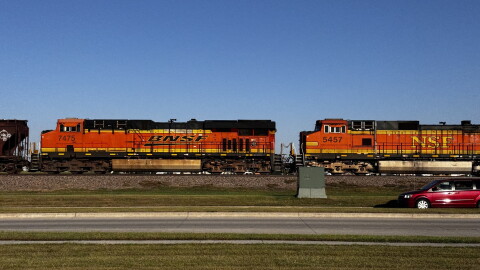 Two orange train cars with the BNSF and NSF logos ride along the train tracks on the side of a road.