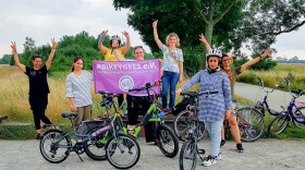 Volunteers and trainees with the group Bikeygees at a park in Berlin in July. The organization teaches refugee women in Germany how to ride bikes. Trainee Shapol Bakir-Rasoul, a refugee from Iraq, holds up a Bikeygees sign with founder Annette Krüger, right. Behind them in yellow is volunteer Shaha Khalef, a refugee from Iraq.