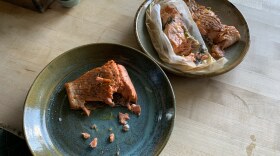 Two plates hold three pieces of salmon. Bites have been taken from each. The plates sit on a wooden countertop.